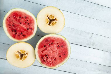 Açık mavi bir ahşap masaya yerleştirilmiş karpuz ve kavun parçaları.