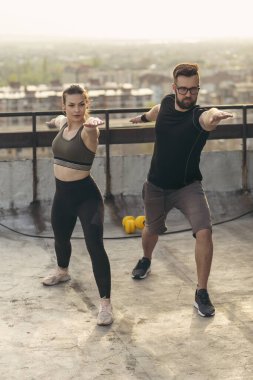 Çalışmadan önce terasta uzanan genç bir çift; arka planda kentsel ufuk çizgisi