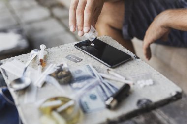 Erkek ellerinin akıllı bir telefon ekranına eroin yerleştirmesi; uyuşturucu bağımlısının eroin koklaması