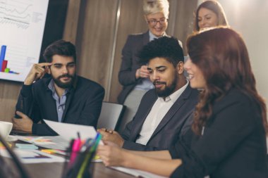 Modern bir ofiste çalışan bir grup iş adamı, sözleşmeleri gözden geçiriyorlar. Ortadaki adama odaklan.