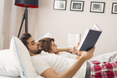 Aşık bir çift uyandıktan sonra yatakta uzanıyor, sarılıyor ve kitap okuyor. Kıza odaklan.