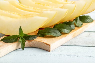 Kesme tahtasında servis edilen soğuk kavun dilimleri, nane yapraklarıyla süslenmiş, yaz tatlısı olarak servis ediliyor.