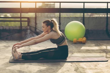 Yoga minderinde oturan genç ve çekici bir kadın antrenmandan önce esniyor.