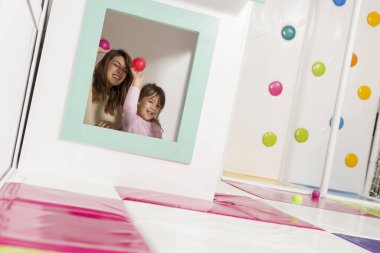 Anne ve kızı oyun odasında oynuyorlar, küçük ahşap bir evde saklanıyorlar, pencereden top atıyorlar.