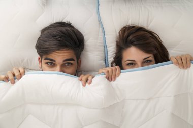 Birbirini seven bir çiftin yatakta yatıp, çarşafların altında saklanıp gözetlediğinin en üst görüntüsü.