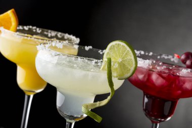 Limonlu margarita, portakallı margarita ve tuz çerçeveli bardaklarda limon, portakal ve vişne ile süslenmiş vişneli margarita karışımı. Limon diliminde FOcus