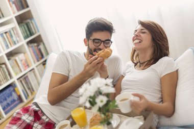 Mutlu çift yatakta uzanıyor, kahvaltı yapıyor ve birlikte vakit geçiriyorlar. Adama odaklan.