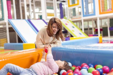 Neşeli anne ve kız renkli toplarla dolu bir havuzda oyun odasında oynuyorlar.
