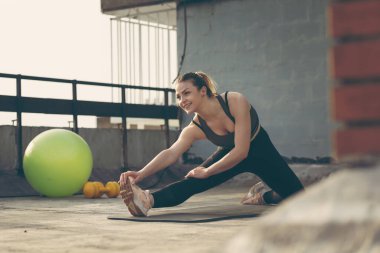 Yoga minderinde oturan genç ve çekici bir kadın antrenmandan önce esniyor.