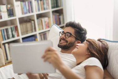 Birbirine aşık çiftler, yatakta yatıyorlar, tablet bilgisayarda internette dolaşıyorlar, haberleri okuyorlar.
