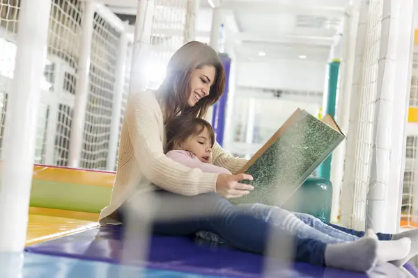 Mother and daughter sitting in a playroom, reading a fairy tale; daughter sitting in mother\'s lap