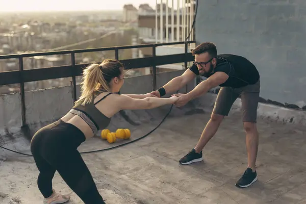 Young couple on a building rooftop terrace stretching before workout; urban skyline in the background