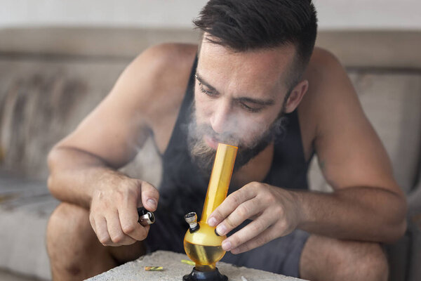 Young man smoking pot using bong; man inhaling marijuana vapor from a bong