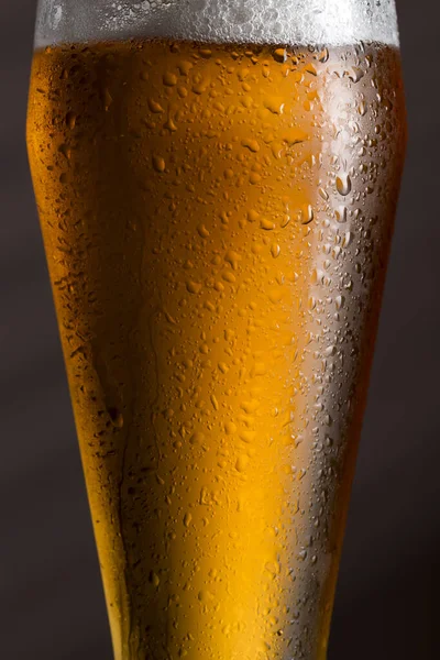 Close up of a wet glass of cold light beer with foam. Selective focus