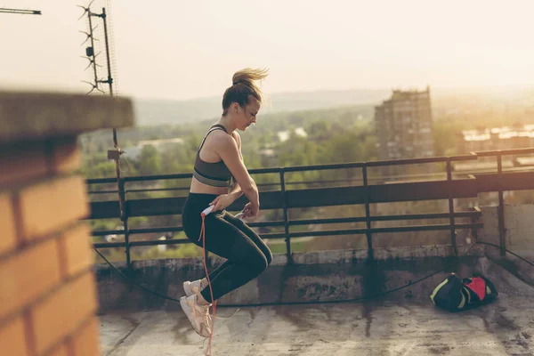 Woman exercising on a building rooftop terrace, doing a cardio training, jumping rope
