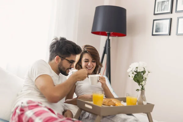 Happy couple in love lying in bed, having breakfast and enjoying their time together