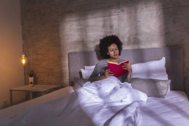 Sabahları pijama giymiş, kitap okuyup rahatlayan güzel, melez bir kadın.