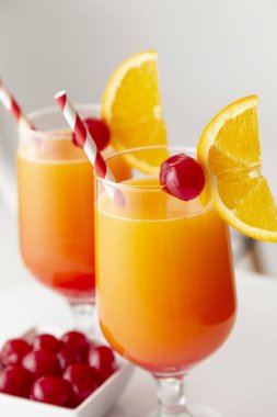 Yüksek açılı iki soğuk tekila kokteyli, tekila, nar suyu ve portakal suyu ile süslenmiş portakal suyu ve maraska kirazı. Camdaki kiraza odaklan.