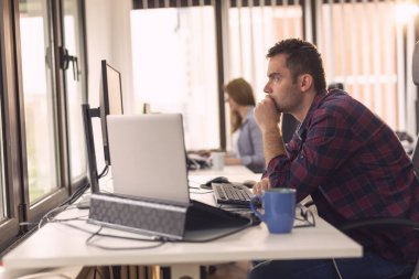İki iş arkadaşı bir ofiste masalarında oturuyor, çalışıyor; yazılım geliştiricileri kodluyor