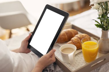 Kadınların elinde beyaz ekranlı siyah bir tablet bilgisayar tutarken yatakta oturup kahvaltı ederken ki görüntüleri. Tablete seçici odaklanma