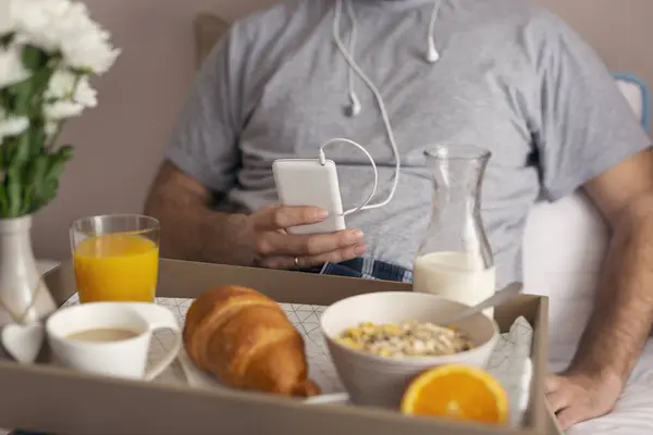 Szczegóły Męskie Ręce Trzymając Smartfon Słuchawkami Słuchając Muzyki Podczas Śniadania — Zdjęcie stockowe