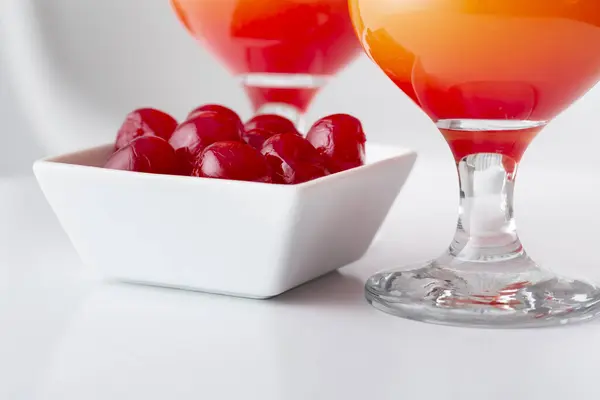 Detail of two cold tequila sunrise cocktails with tequila, pomegranate juice and orange juice decorated with slices of orange and maraschino cherries. Selective focus on the cherries