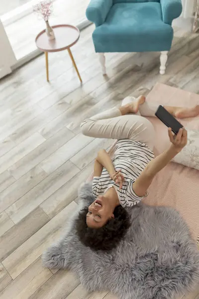 Güzel Bir Melez Kadının Oturma Odasında Yerde Yatıp Akıllı Telefonuyla — Stok fotoğraf