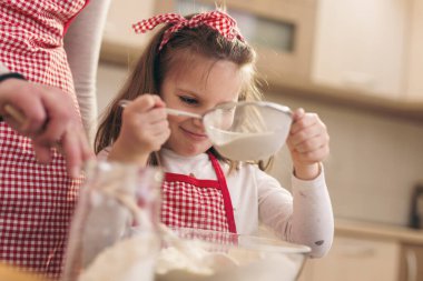 Anne ve kızı kevaşenin içine un ekiyorlar. Anne kızına hamur yoğurmayı öğretiyor.
