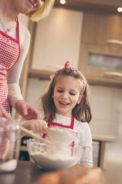 Anne ve kızı kevaşenin içine un ekiyorlar. Anne kızına hamur yoğurmayı öğretiyor.