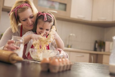 Güzel küçük kız annesinin yardımıyla hamur yoğuruyor, mutfakta eğleniyor.