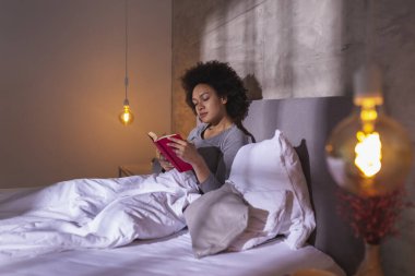 Sabahları pijama giymiş, kitap okuyup rahatlayan güzel, melez bir kadın.