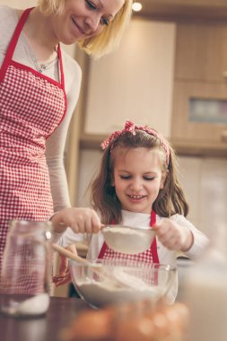 Anne ve kızı kevaşenin içine un ekiyorlar. Anne kızına hamur yoğurmayı öğretiyor. Kızına odaklan.