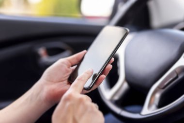 Akıllı bir telefonu tutan ve arabada otururken mesaj yazan kadın ellerinin ayrıntıları; yolun kenarına park edin ve güvenli bir şekilde akıllı telefon kullanın; trafik güvenliği kavramı