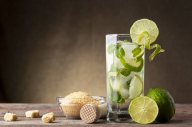 Bol buzlu mojito kokteyli, beyaz rom, limon suyu ve tonik, limon dilimleri ve kırsal ahşap bir masada naneli yapraklarla süslenmiş.