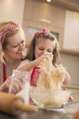 Annesinin yardımıyla hamur yoğurup mutfakta eğlenen güzel küçük kız.