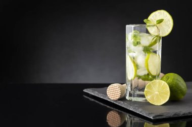 Bol buzlu mojito kokteyli, beyaz rom, limon suyu ve tonik, limon dilimleri ve nane yapraklarıyla süslenmiş siyah taş tepside.