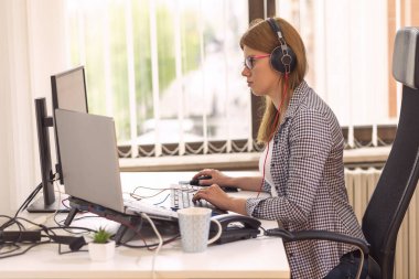 Ofisteki bir masada oturan çağrı merkezi operatörü, kulaklık takıyor ve telefonlar alıyor.