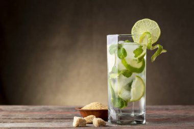 Bol buzlu mojito kokteyli, beyaz rom, limon suyu ve tonik, limon dilimleri ve kırsal ahşap bir masada naneli yapraklarla süslenmiş.