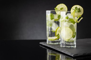 Beyaz rom, limon suyu ve limon dilimleri ve nane yapraklarıyla süslenmiş bir bardak soğuk mojito kokteyli.