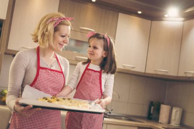 Anne ve kızı mutfakta, fırın tepsisinde pizza pişirmeye hazırlar. Kızına odaklan.