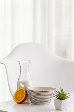 Sağlıklı bir kahvaltı olarak sunulan bir kase mısır gevreği, süt şişesi ve taze portakal. Kaseye odaklan.