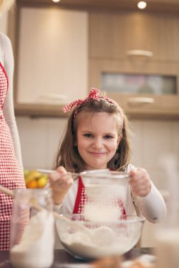 Anne ve kızı kevaşenin içine un ekiyorlar. Anne kızına hamur yoğurmayı öğretiyor.