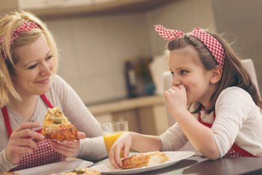 Anne ve kızı mutfakta oturuyor, pizza yiyor ve eğleniyor. Kızına odaklan.