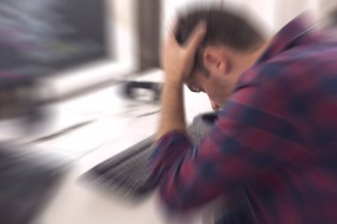 Genç yazılım geliştiricisi iş yerinde masasında oturuyor, el ele tutuşuyor, arıza ve kod arızası yüzünden strese giriyor.