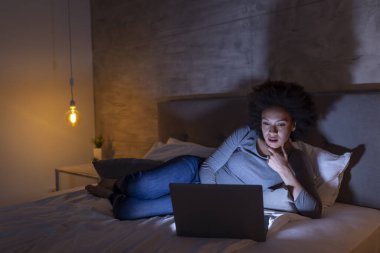 Güzel, genç, melez bir kadın gece geç saatlere kadar çalışıp dizüstü bilgisayar kullanıyor.