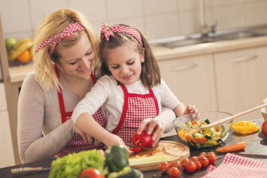 Anne ve kızı sebze doğruyor ve salata yapıyorlar. Kızına odaklan.