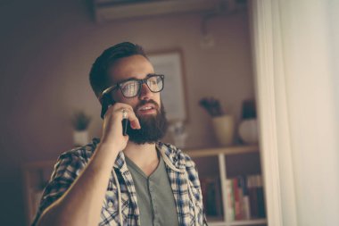 Neşeli genç adam akıllı telefonuyla telefon görüşmesi yapıyor.