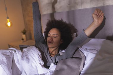 Sabahları pijama giyen güzel, melez bir kadın uyanıp evde dinleniyor.