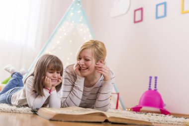 Anne ve kızı oyun odasında yerde yatıp masal okuyorlar. Annesine odaklan.