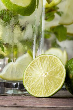 Beyaz rom, limon suyu ve limon dilimleri ve nane yapraklarıyla süslenmiş tonik ile birlikte soğuk mojito kokteyli. Limonun yarısına odaklan.